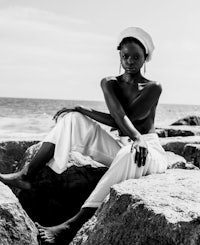 black and white photo of a woman sitting on rocks by the ocean