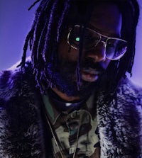 a man with dreadlocks and glasses in front of a purple background