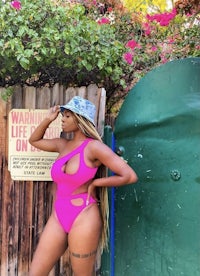 a woman in a pink swimsuit posing in front of a fence
