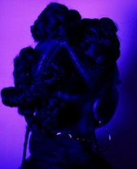 the back of a woman with braids in front of a purple light