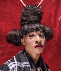 a woman with long hair and a hat is posing in front of a red wall