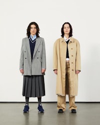 two women in trench coats and skirts standing next to each other
