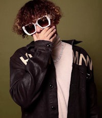 a man with curly hair wearing sunglasses and a leather jacket