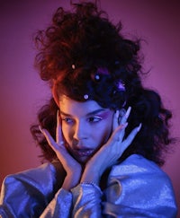 a woman with curly hair posing in front of a purple background