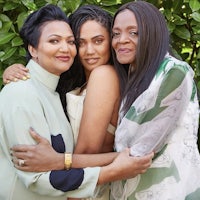 three women hugging each other in front of bushes