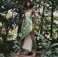 a black woman in a green dress standing on a log in the woods