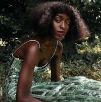 a black woman in a green dress sitting in the grass