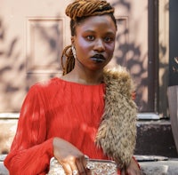 a black woman wearing a red dress and a fur clutch